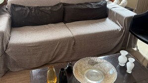 Een woonkamer met een bank, een bijzettafeltje met decoratieve objecten, en een raam met een glas-in-lood ontwerp.
