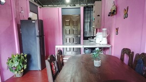 Un comedor con una mesa y sillas de madera, un refrigerador, una planta en maceta y una cocina al fondo.