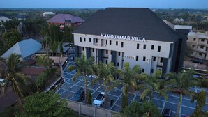 A building named 'KAMOJAMAS VILLA' with a flat roof, multiple windows, and a parking area with palm trees. - Kamojama Villa (Abakaliki)