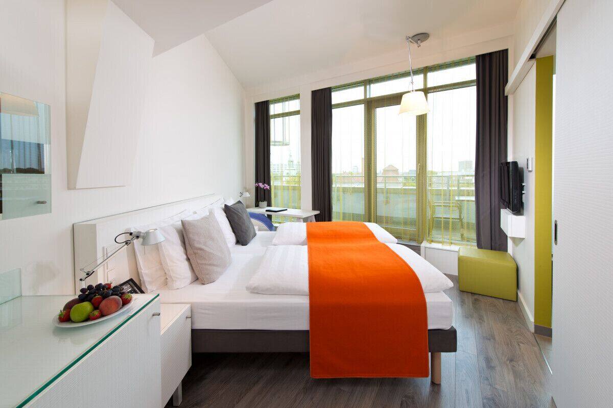 Ein modernes Hotelzimmer mit Bett, Nachttisch und großem Fenster.