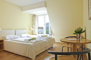 Hotellihuone, jossa on sänky, pöytä, tuoli ja ikkuna, josta on näkymä.