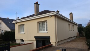Un edificio residenziale su due piani con facciata beige, due camini e un piccolo portico.