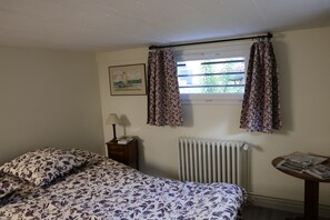 A bedroom with a bed, a nightstand with a lamp, a radiator, a window with curtains, and a framed picture on the wall. - SLEEP JUST A STONE'S THROW FROM THE LOIRE BY BIKE! (Orléans)