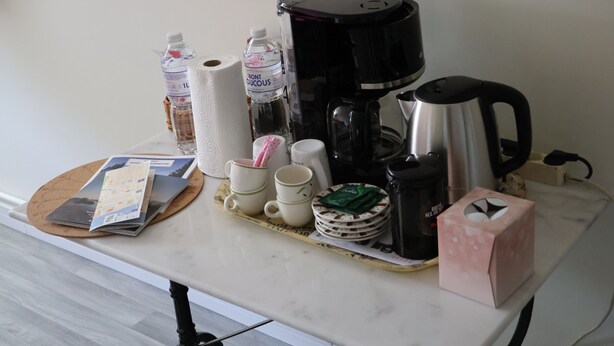 Un tavolo con una macchina del caffè, bottiglie d'acqua, tazze, un rotolo di fazzoletti, una mappa e un box di fazzoletti.