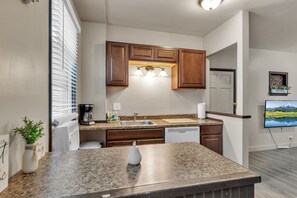 Una cocina moderna con encimeras de granito, armarios de madera, lavavajillas integrado y una ventana con persianas.