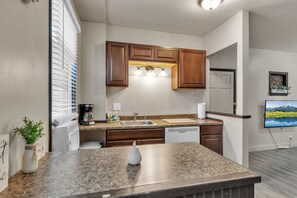 A modern kitchen with granite countertops, wooden cabinets, a built-in dishwasher, and a large window with blinds. - Niagara Falls Getaway (Niagara Falls)