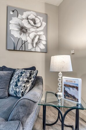 A living room with a grey sofa, a geometric patterned pillow, a wall-mounted lamp, and a framed welcome sign. - Niagara Falls Getaway (Niagara Falls)
