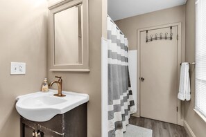 Un baño con lavamanos, espejo, toallero y cortina de ducha.