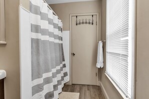 A bathroom with a shower curtain, a towel rack, a door, and a window with blinds. - Niagara Falls Getaway (Niagara Falls)
