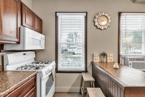 A kitchen with a stove, oven, wooden cabinets, a window with blinds, a clock, and a countertop with a vase and signs. - Lovely 2-bedroom townhome in Niagara Falls (Niagara Falls)