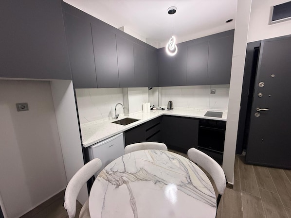 A modern kitchen with dark cabinets, a white countertop, and a marble dining table.
