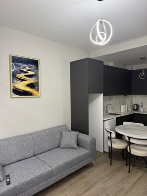 A modern living space with a grey sofa, a dining table with chairs, a kitchen area, and a ceiling light fixture. - BOSS LOUNGE (Eskişehir)