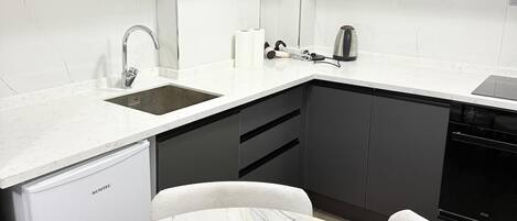 A modern kitchen with grey cabinets, a white countertop, a marble dining table, and a coffee maker.