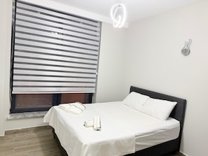 Un dormitorio con cama, ventana con persianas, una toalla y un aplique de pared.