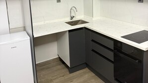 Cocina compacta con gabinetes grises, encimera blanca, lavavajillas integrado y refrigerador blanco.