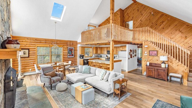 Un intérieur spacieux de chalet en bois, comprenant un coin repas, un salon, une cuisine et une chambre à l’étage, accessible par un escalier en bois.