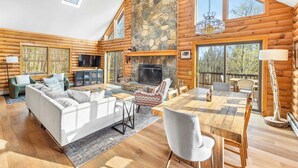 L’intérieur d’une cabane en rondins, avec une cheminée en pierre, une table à manger en bois et une grande fenêtre donnant sur l’extérieur.