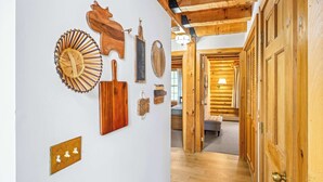 Un intérieur en bois avec un couloir menant à une pièce, comprenant un luminaire fixé au mur et une porte dotée d’une poignée en laiton.