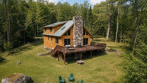 Une cabane dotée d’une cheminée en pierre, d’une terrasse en bois et d’un espace salon extérieur.