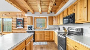 Une cuisine rustique aménagée dans une cabane en rondins, avec des meubles en bois, un réfrigérateur en acier inoxydable, un four à micro-ondes et une cuisinière.