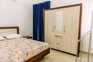 Ein Schlafzimmer mit einem Bett, einem Kleiderschrank, einem Nachttisch und einem Badezimmer mit Duschvorhang.