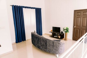 Ein Wohnzimmer mit einer Couch, einem Fernseher, einer Pflanze und einer Tür.