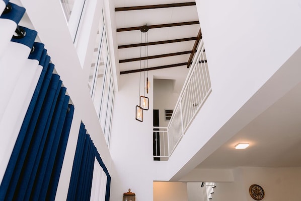 Un intérieur à plusieurs niveaux, avec des murs blancs, un plafond en bois et une rambarde blanche.