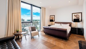 A modern hotel room with a large bed, a seating area, a small table, and a view of the city. - Luxury 4-Bed Duplex Penthouse (London)