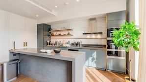 A modern kitchen with a central island, white cabinets, and a potted plant. - Luxury 4-Bed Duplex Penthouse (London)