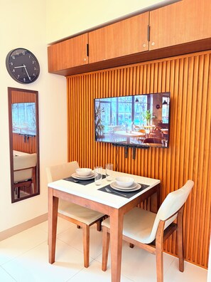 Un comedor con una mesa de madera, sillas, un reloj y un televisor montado en una pared de madera.