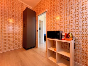 Ein Flur mit gemustertem Wandpapier, einem Kleiderschrank, einer Mikrowelle und einer Kaffeemaschine auf einem Regal.