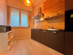Eine moderne Küche mit Mikrowelle, Herd und Spüle, Holzschränken und einem Fenster mit Jalousien.