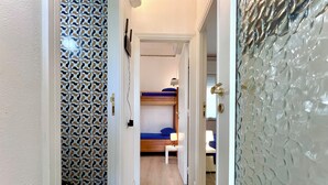 A hallway with patterned wallpaper, a bunk bed room, and a door with textured glass. - Poetto Beach | 5 Min Walk [WiFi & AC] (Cagliari)