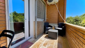 A balcony with a sliding glass door, two wicker chairs, a small table, a wicker ottoman, and a ceiling fan. - Poetto Beach | 5 Min Walk [WiFi & AC] (Cagliari)