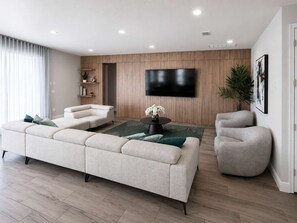 Ein modernes Wohnzimmer mit einer Eckcouch, einem runden Couchtisch, einem grauen Sessel und einem flachbildfernseher, der an der Wand befestigt ist.