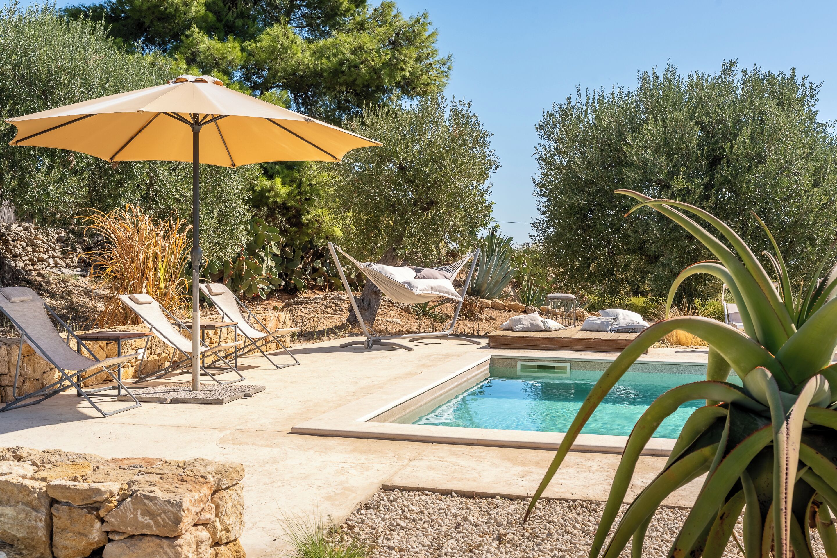 Uma área de piscina com espreguiçadeiras, uma rede e um guarda-sol.