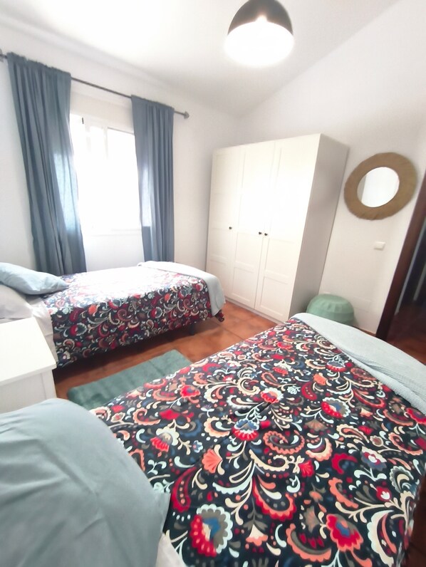 A room with two beds, a wardrobe, a round mirror, and a window with curtains.