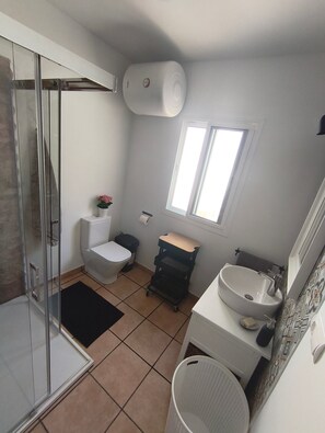 A bathroom with a shower, toilet, sink, and a small window.