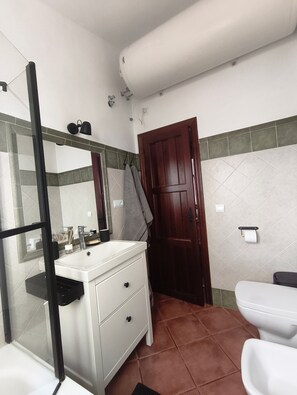 A bathroom with a white sink, mirror, and toilet, a wooden door, and tiled walls.