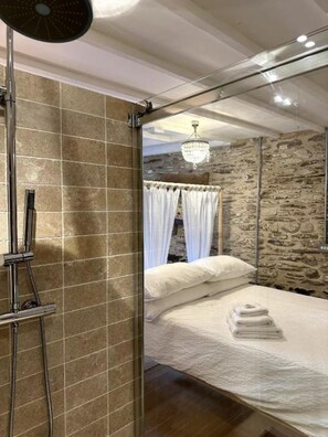 Ein Schlafzimmer mit Dusche, einem Bett mit weißer Bettwäsche, einer Chandelüster und Steinwänden.