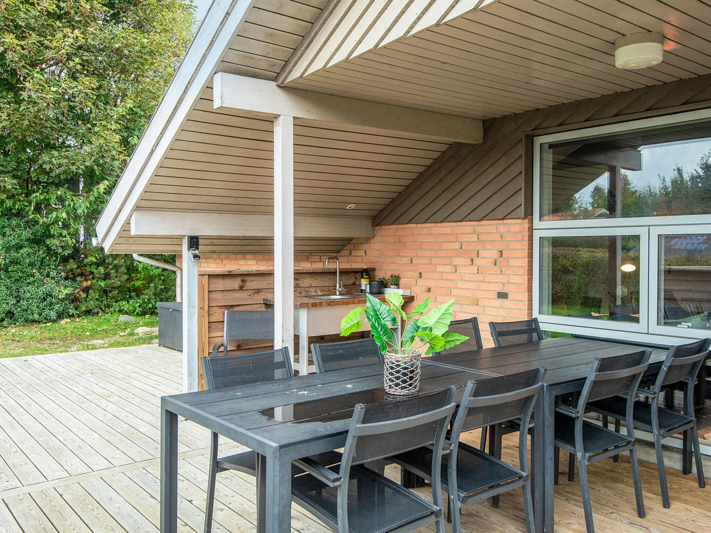 An outdoor patio with a dining table and chairs, a brick wall, and a large window.