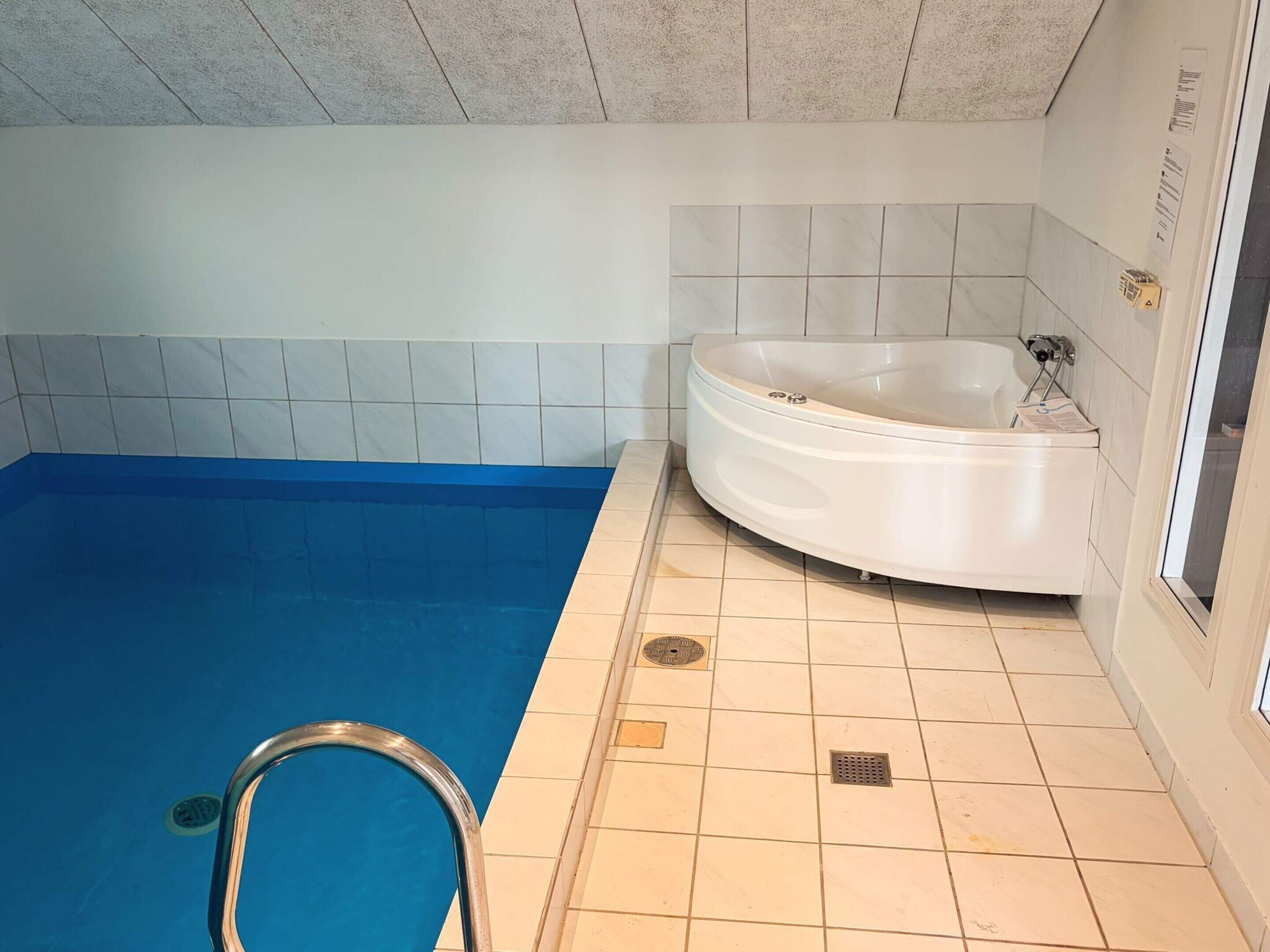Uma piscina com piso azul, banheira branca e paredes revestidas de azulejos.