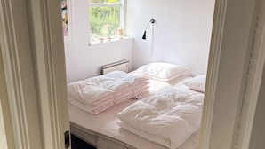 A bedroom with a bed, pillows, a bedside lamp, a window with a view of greenery, and a radiator. - 4 Star Holiday Home in Juelsminde (Horsens)