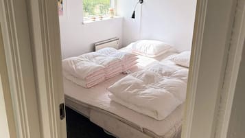 Quarto com cama, almofadas, abajur, janela com vista para área verde e radiador.