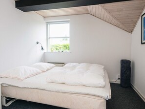 A single bed with a white mattress and pillows, a window with a view of greenery, a wall-mounted lamp, and a dark-colored bag on the floor. - 4 Star Holiday Home in Juelsminde (Horsens)