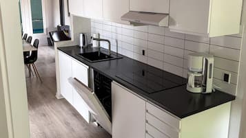 Cozinha moderna com armários brancos, bancada preta, lava-louças embutida e cafeteira.