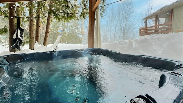 A hot tub under a wooden structure with snow outside. - Le Nordique | Private Sauna & Spa | Lake access (Val-des-Lacs)