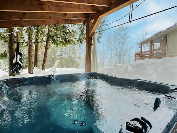 A hot tub under a wooden structure with snow outside. - Le Nordique | Private Sauna & Spa | Lake access (Val-des-Lacs)