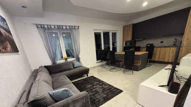 A modern living room with a sofa, a rug, and a kitchen area with a counter and chairs.