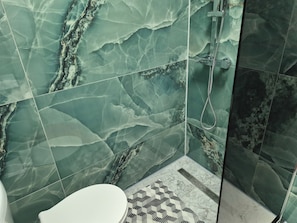 Ein Badezimmer mit grünen Marmorfliesen, einer weißen Toilette und einem gemusterten Boden.